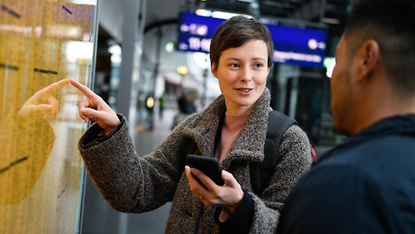 Frau zeigend auf Fahrplanaushang am Gleis