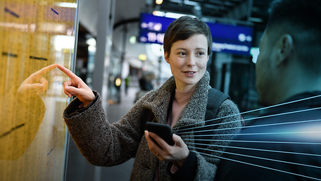 Frau zeigend auf Fahrplanaushang am Gleis