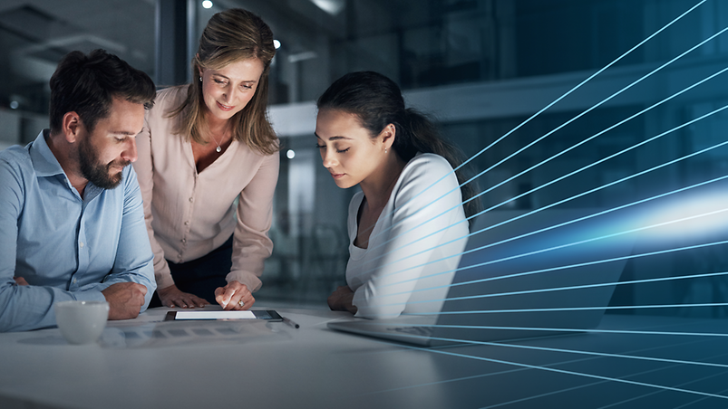 Ein Mann und zwei Frauen in einem Meeting auf ein Tablet blickend