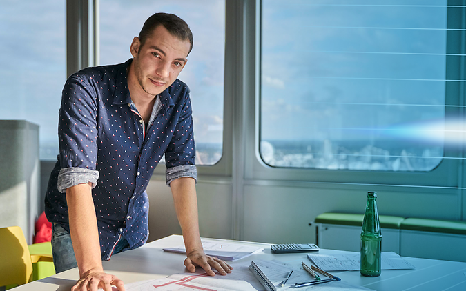 Junger Mann im Büro stehend an einem Schreibtisch