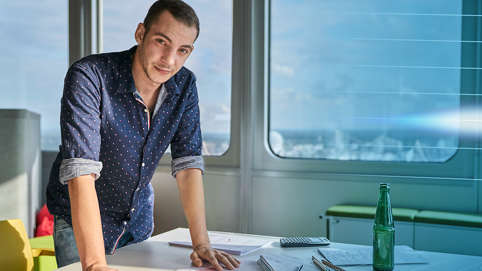 Junger Mann im Büro stehend an einem Schreibtisch