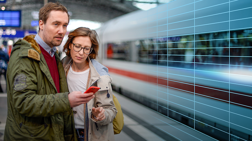 A man and a woman standing on a railway track next to an ICE train with a smartphone in their hands