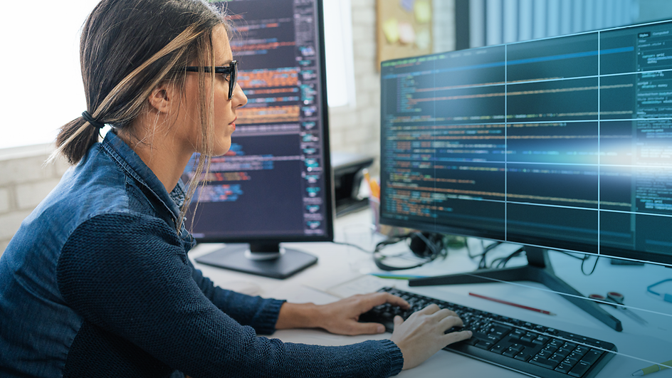 A woman sitting in front of two screens showing code