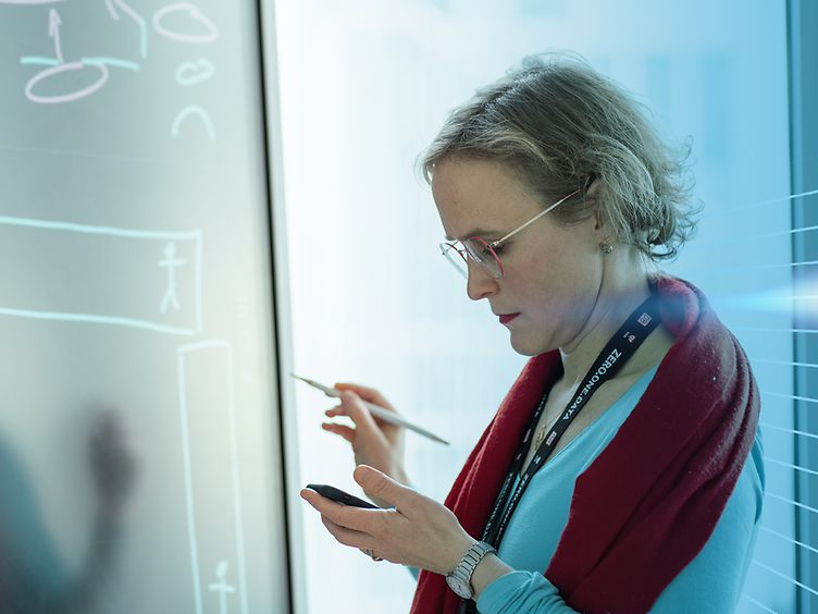 Laura Hinsch mit Smartphone und Stift in der Hand stehend vor einem Screen