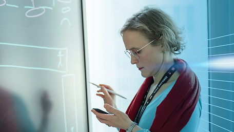 Laura Hinsch mit Smartphone und Stift in der Hand vor einem Display