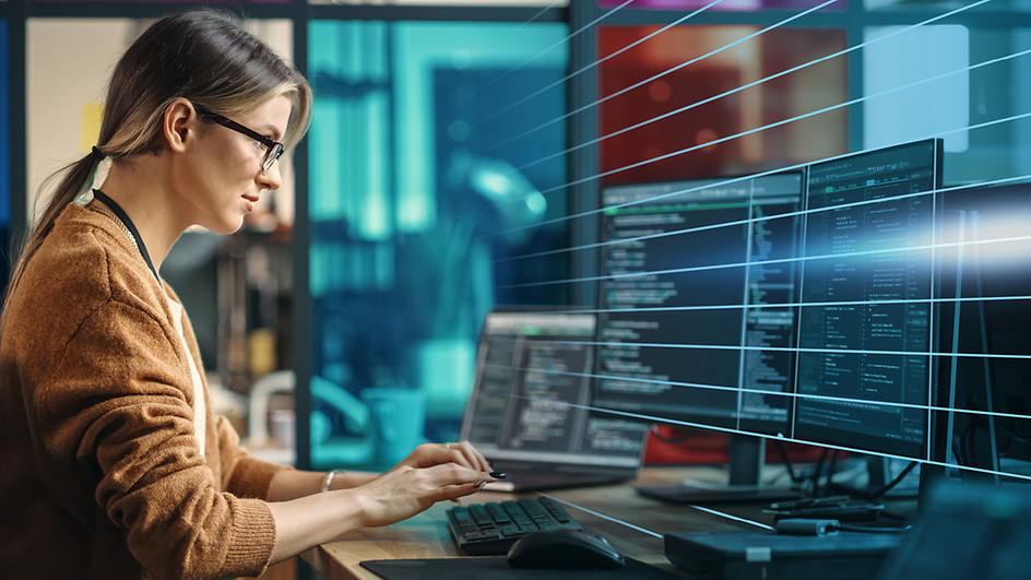 Frau mit Brille an Schreibtisch sitzend vor Bildschirmen mit Code