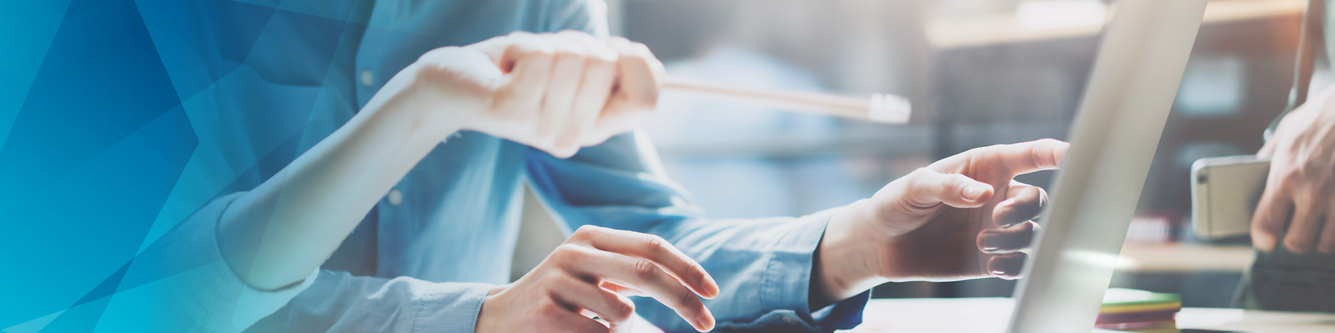 Two people sitting in front of a laptop. One hand holds a pen.