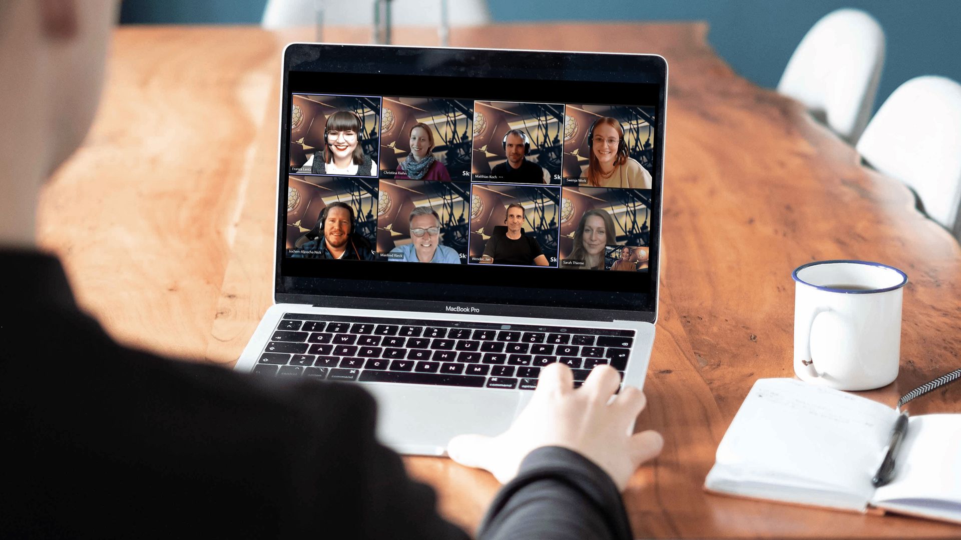 Person sitzend am Tisch vor einem Laptop mit einer MS-Teams Besprechung