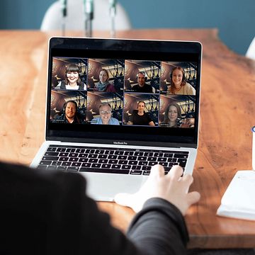 Person sitzend am Tisch vor einem Laptop mit einer MS-Teams Besprechung