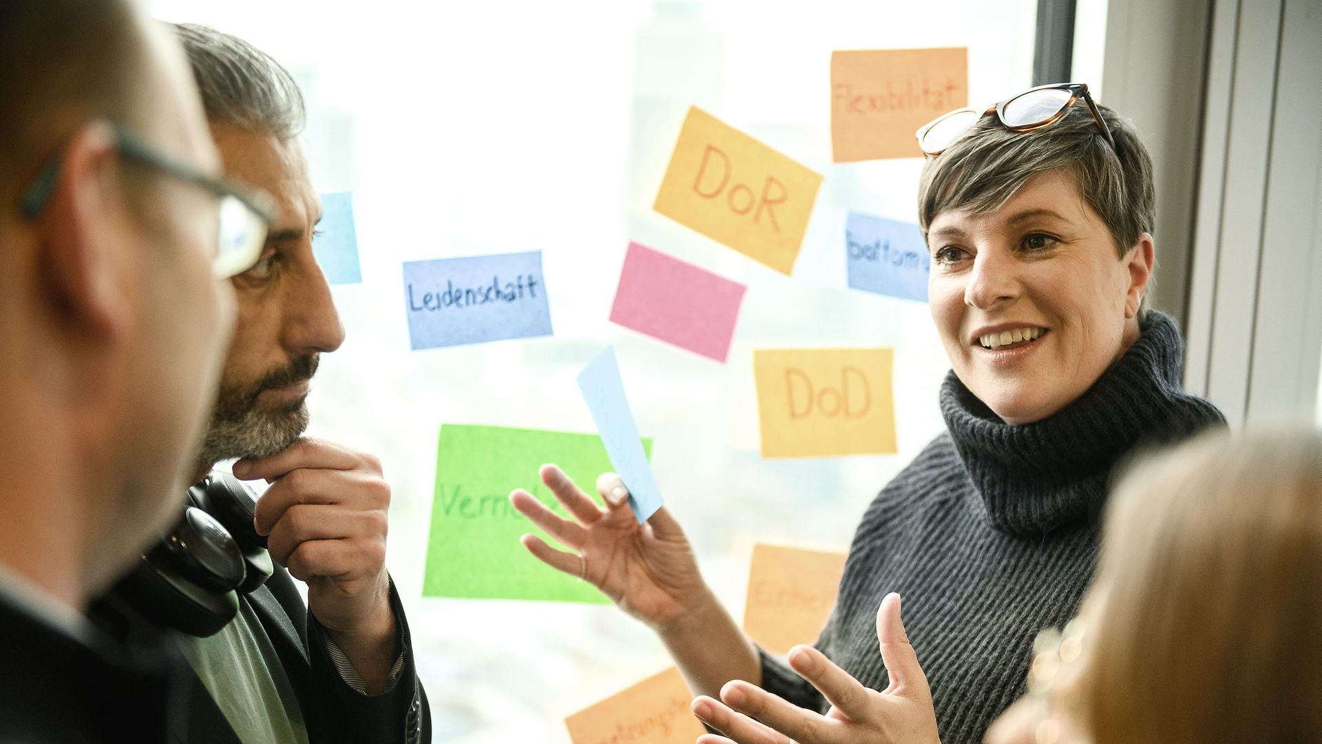 Woman explaining in front of window on which various colourful stickers are hanging