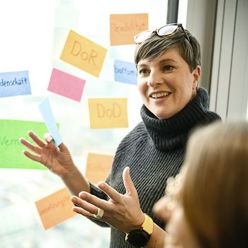 Woman explaining in front of window on which various colourful stickers are hanging